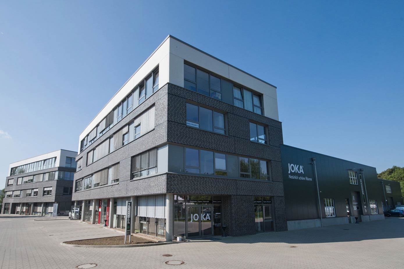  Gewerbehof bestehend aus zwei Gebäuden, die viele Fenster aufweisen, mit einem geparkten Auto im Vordergrund.