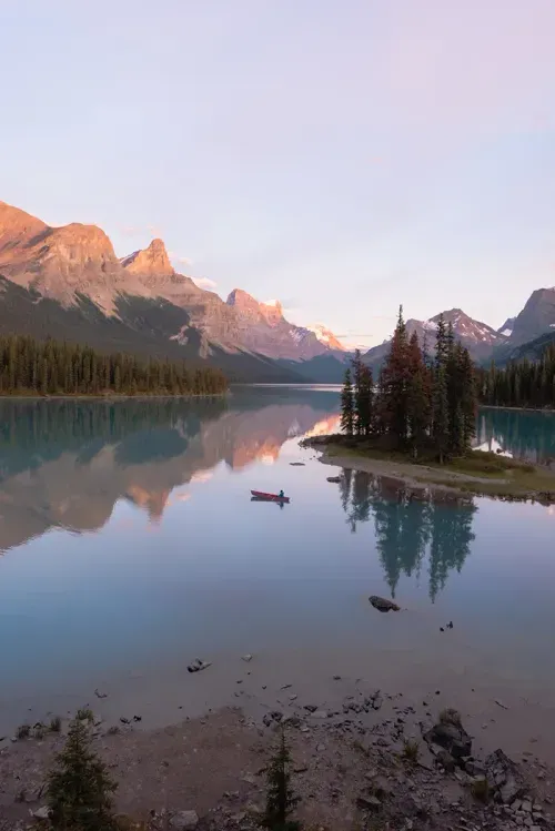 Landscape of Lake Louise in Canada with glossy water, canoer, small island, and snow capped mountains in the background