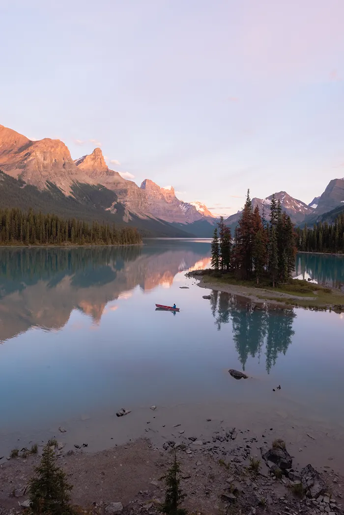 Landscape of Lake Louise in Canada with glossy water, canoer, small island, and snow capped mountains in the background