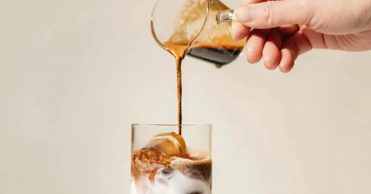 Hand pouring espresso into iced coffee drink, edited on VSCO