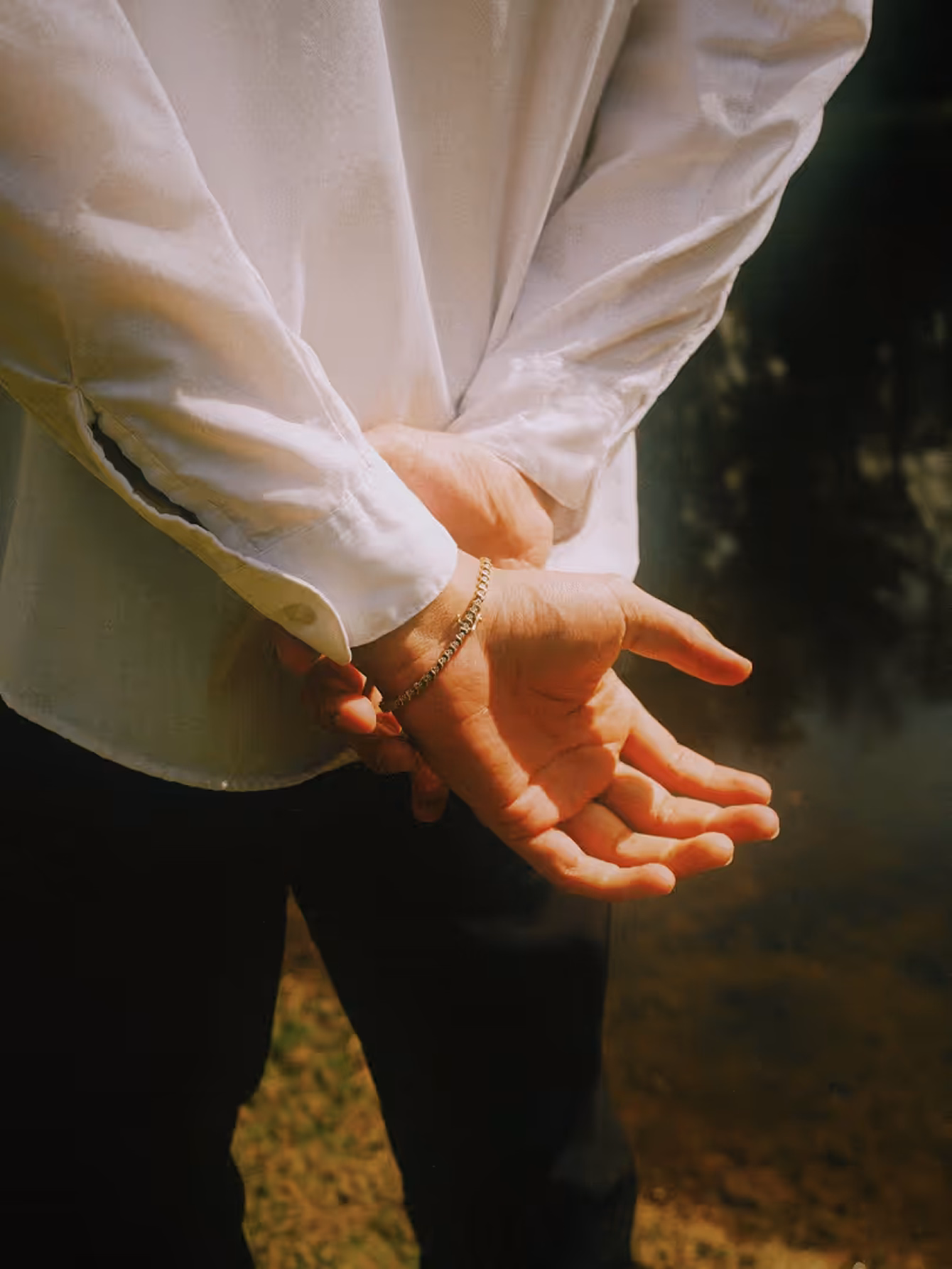 Person standing in white long sleeve shirt with hands behind back in warm lighting