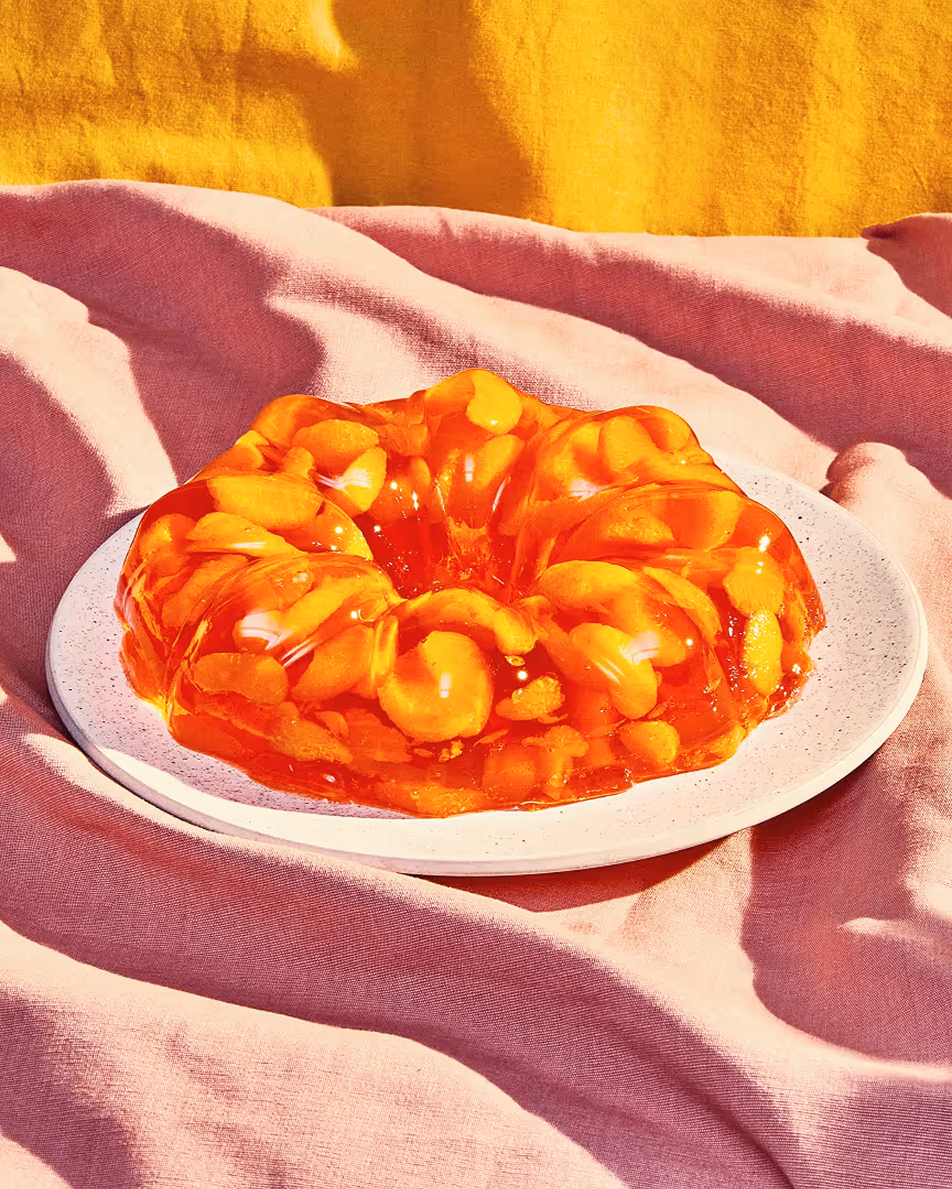 Orange Jello mold on a speckled plate with pink and yellow linen backdrop cloth taken by photographer Cody Guilfoyle