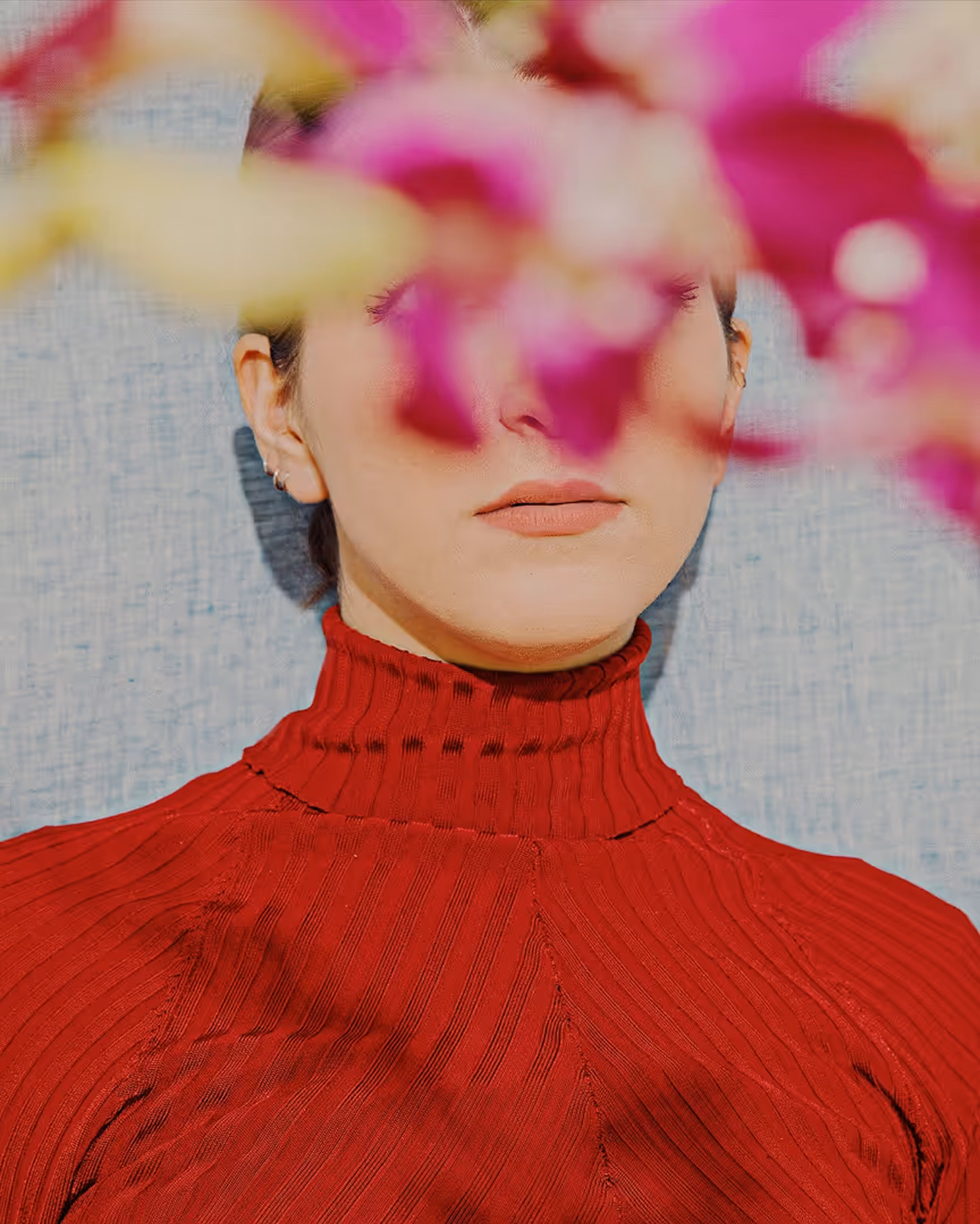 Portrait photo of a woman in a red turtleneck sweater with face covered by out of focus pink flowers taken by Cody Guilfoyle