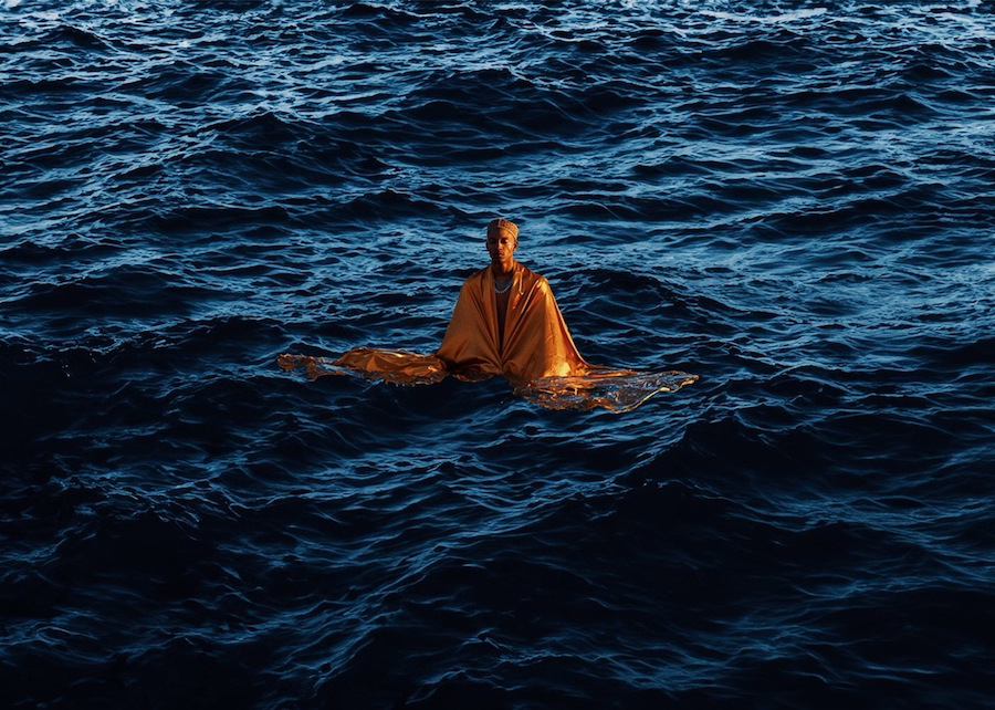 Image of a man sitting on top of the deep blue ocean by John Baloy