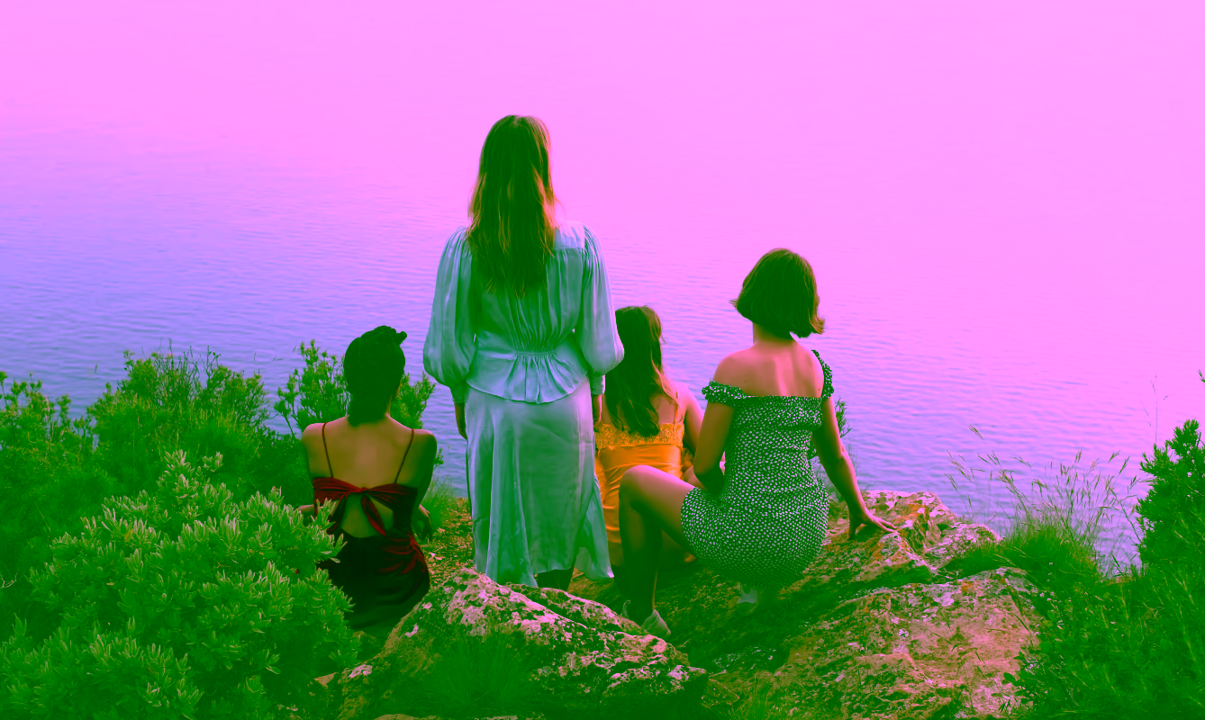 Group of women in colorful dresses facing out towards water