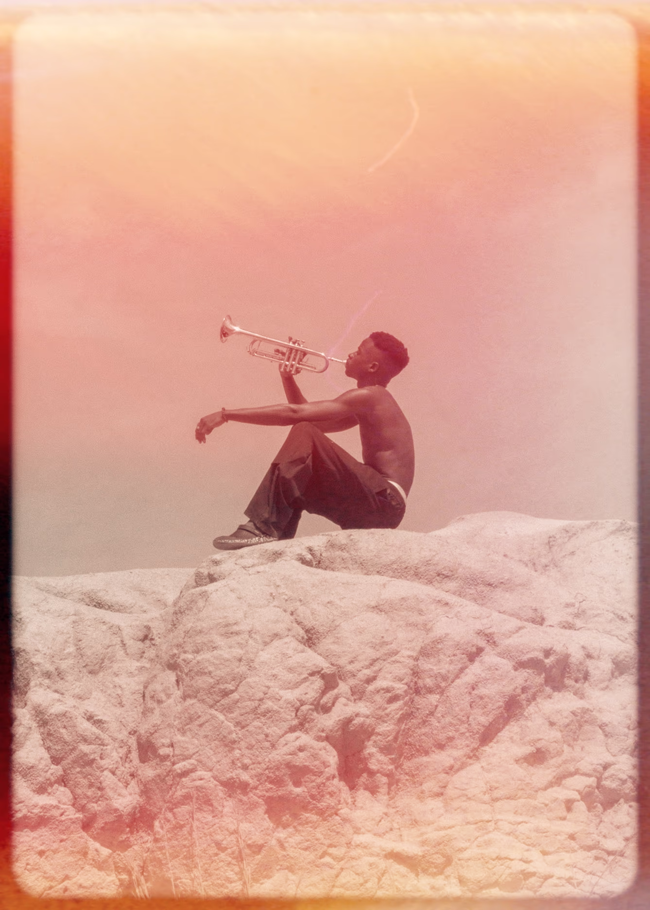 Distressed photo of a man sitting on a large rock holding a trumpet
