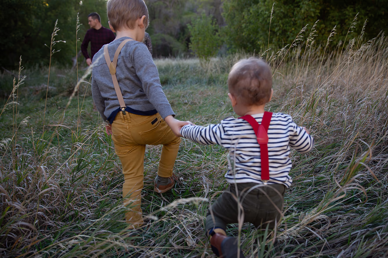 Two kids holding hands in a tall grass field during family photos mini session with a professional photographer