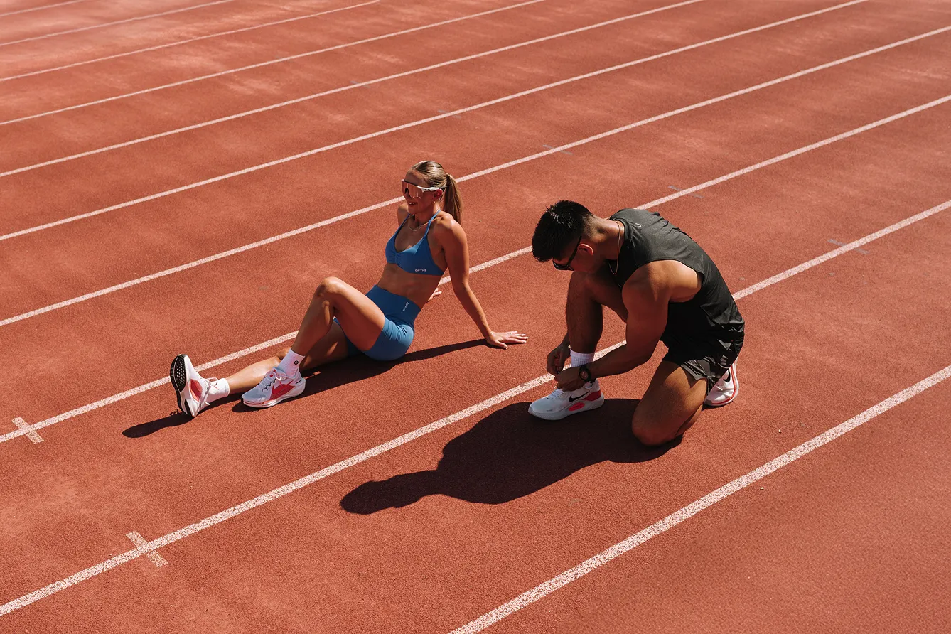 Fitness industry photoshoot of two runners on a track, one sitting own and one tying shoe