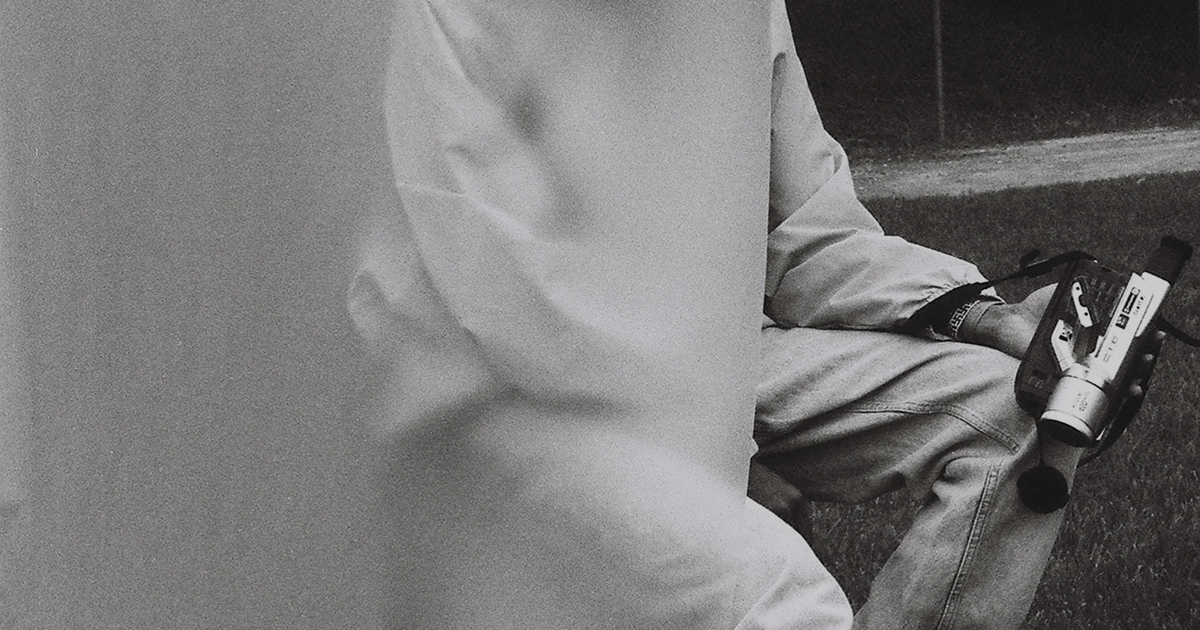 Foto analógica en blanco y negro de una persona con chamarra blanca y jeans sosteniendo una videocámara, con el logotipo de VSCO Workspace