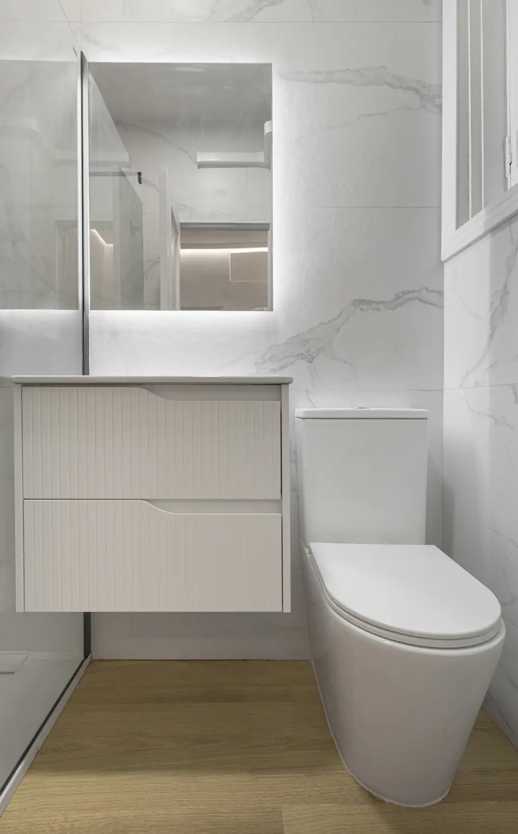 Baño blanco compacto con mueble lacado y mampara transparente