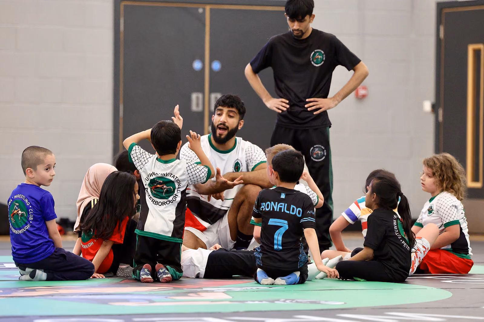 Kids sit around a teacher on a wrestling mat at Gladstone Community centre