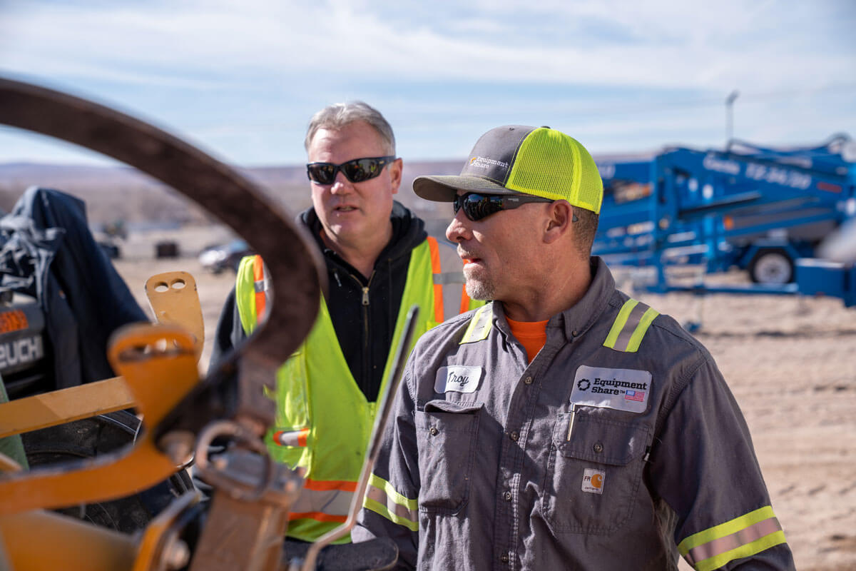 two men wearing hi-vis clothing inspecting some heavy equipment.