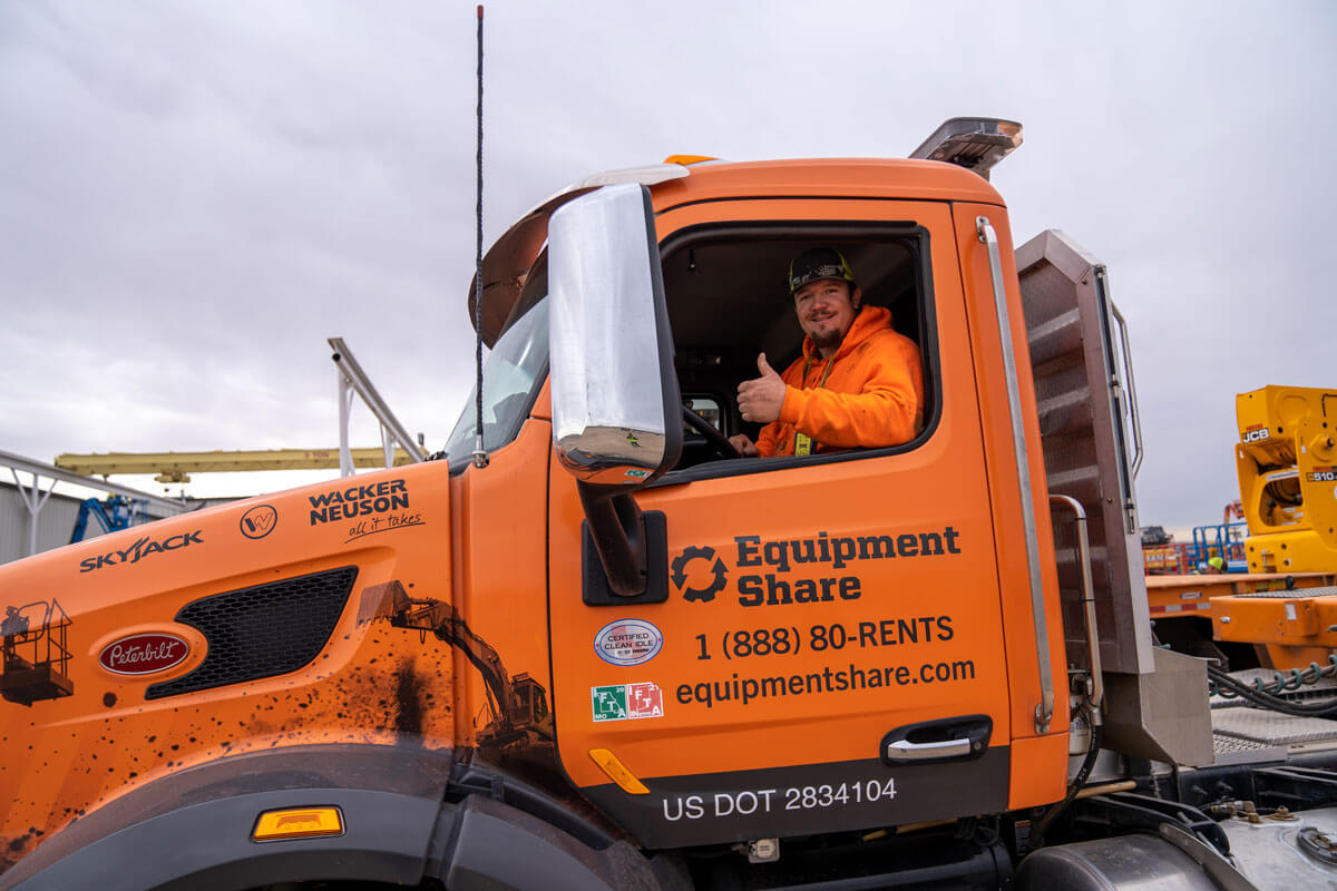 Equipmentshare Driver in an orange EquipmentShare truck giving a thumbs up