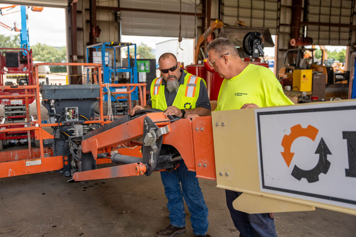 Two EquipmentShare Technicians examine a boom lift.