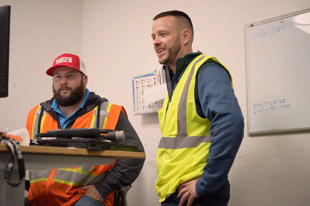 Two men wearing hi-vis clothes and smiling.