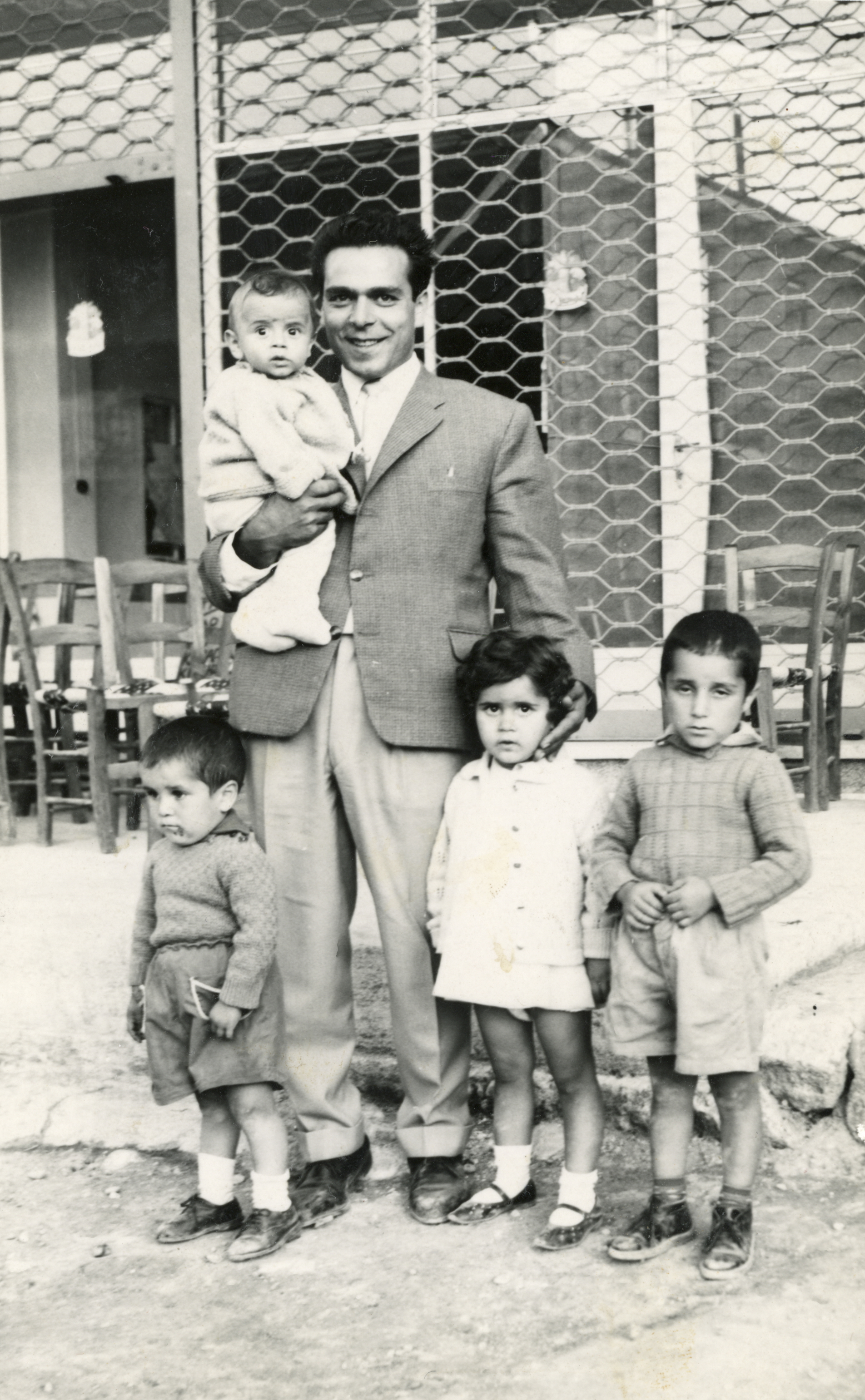 Theodoros outside of his uncle's coffee shop in Kyperounda with his son, daughter, and nephews, 1963 