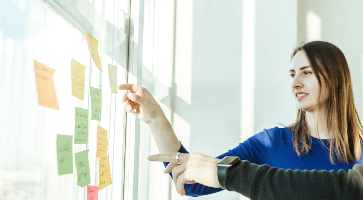Two people pointing at a board with sticky notes