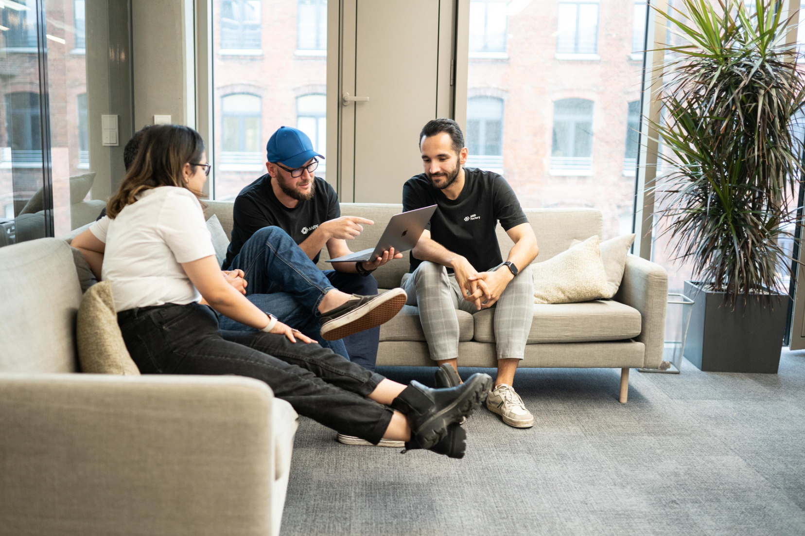 Three men and a Woman sitting on two couches and talking, showing something on a computer