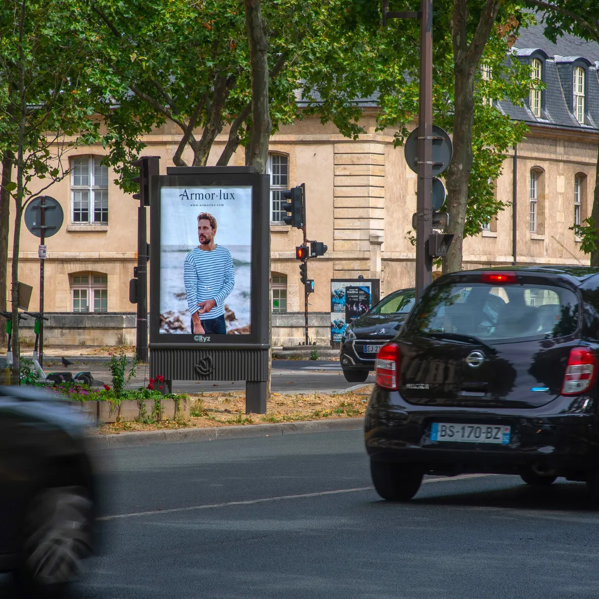 Outdoor street ad with a man in a striped shirt on a display near traffic lights and parked cars.