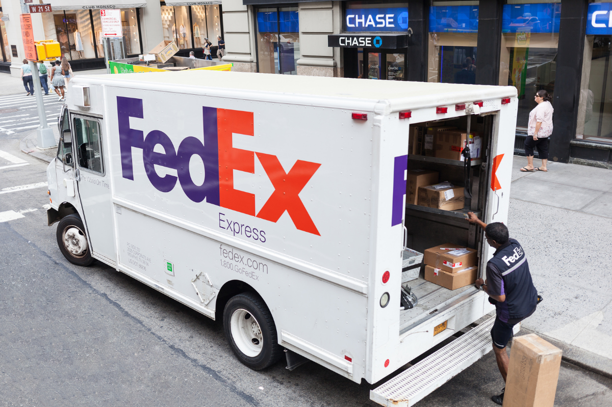 A worker removing packages from the back of a FedEx delivery truck.