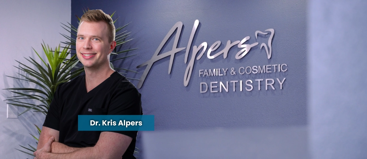 Dr. Kris Alpers standing in front of Alpers Family and Cosmetic Dentistry office sign. Text says they offer invisalign, veneers and other cosmetic and restorative treatment options in Scottsdale, AZ.