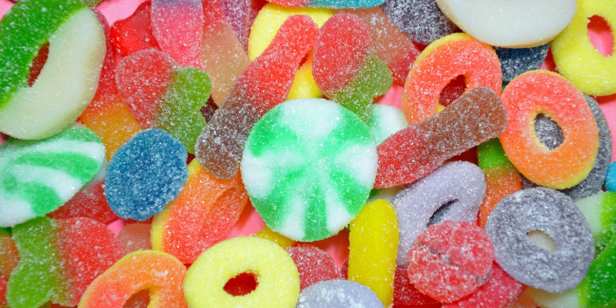Assorted colorful sour gummy candies coated in sugar, including gummy rings and chewy fruit shapes.