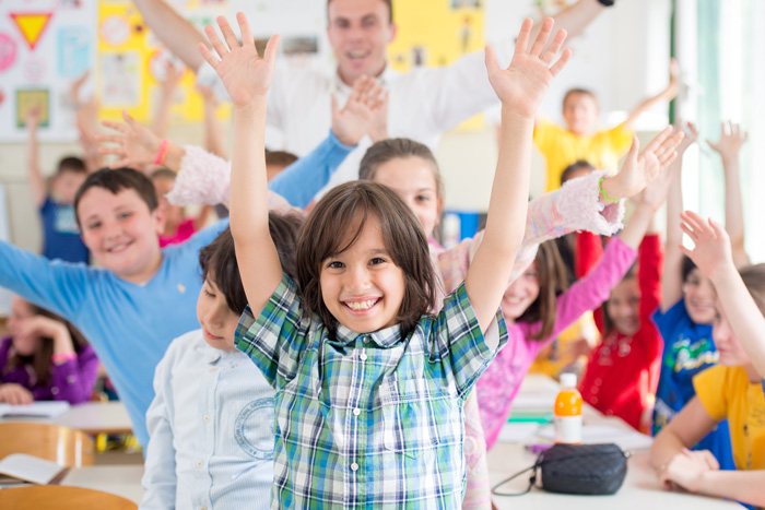 Un groupe d'enfants dans une salle de classe lève la main.