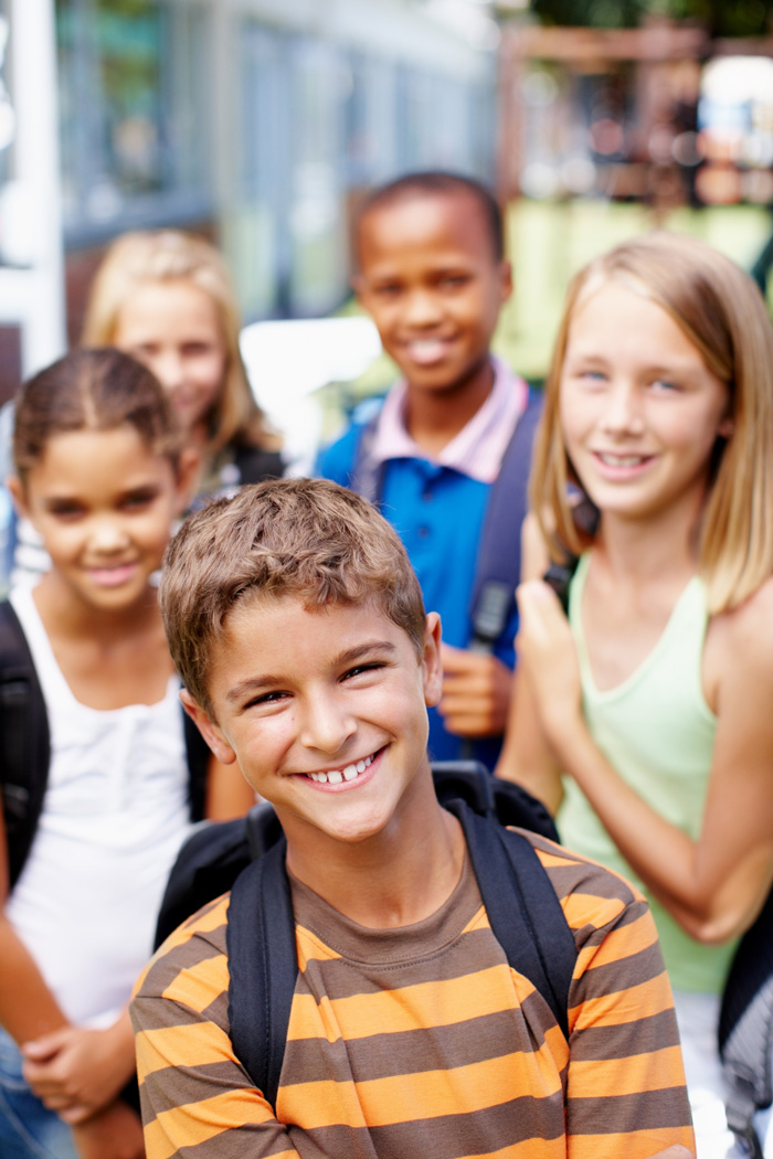 Un groupe d'enfants avec des sacs à dos debout devant un bâtiment scolaire.