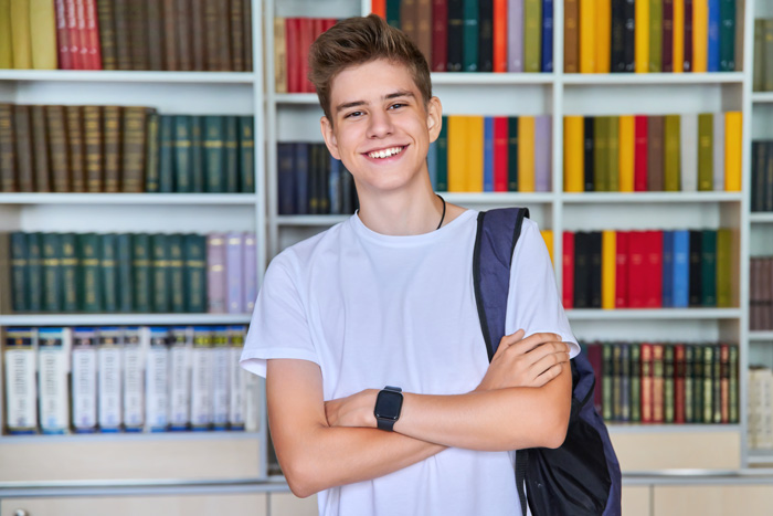 Un jeune homme les bras croisés devant une bibliothèque.