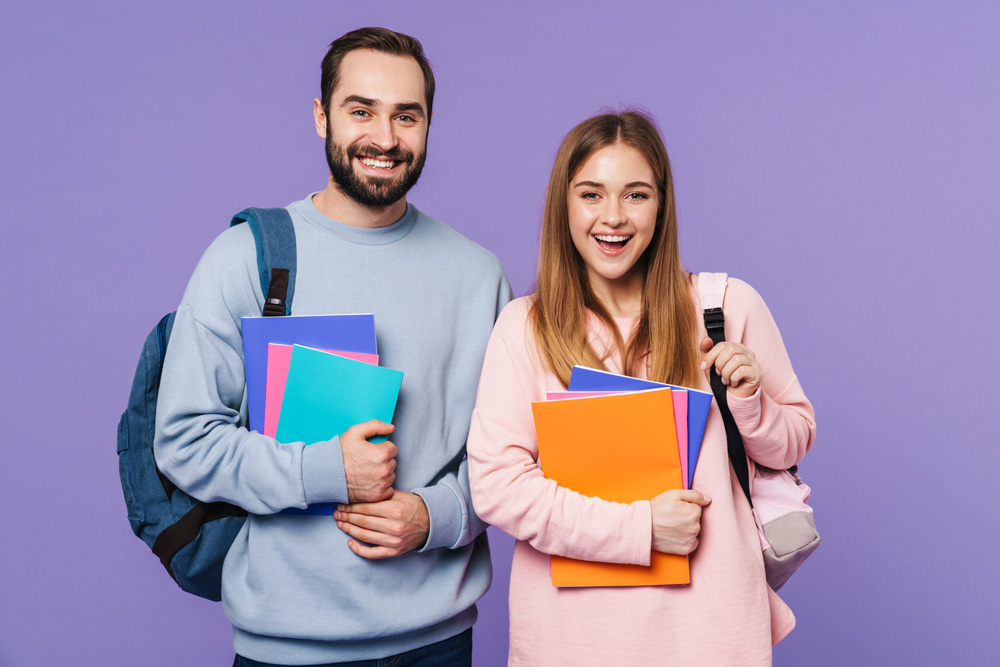 Un jeune couple tenant des sacs à dos et des livres sur fond violet.