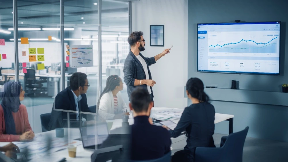 People sat around a desk watching a PowerPoint presentation