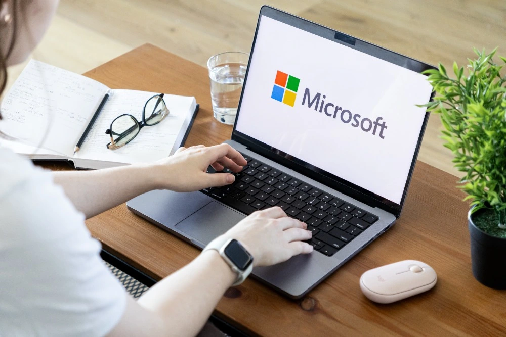 A photo of a woman using a laptop displaying the Microsoft logo