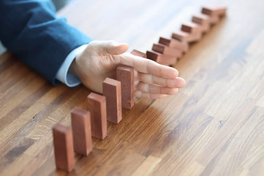Homem empurrando peças de dominó em queda, representando os 4 tipos de riscos financeiros e como evitá-los.