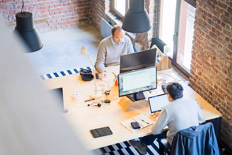 Duas pessoas no escritório trabalhando, em uma mesa, e lendo no computador sobre SaaS.