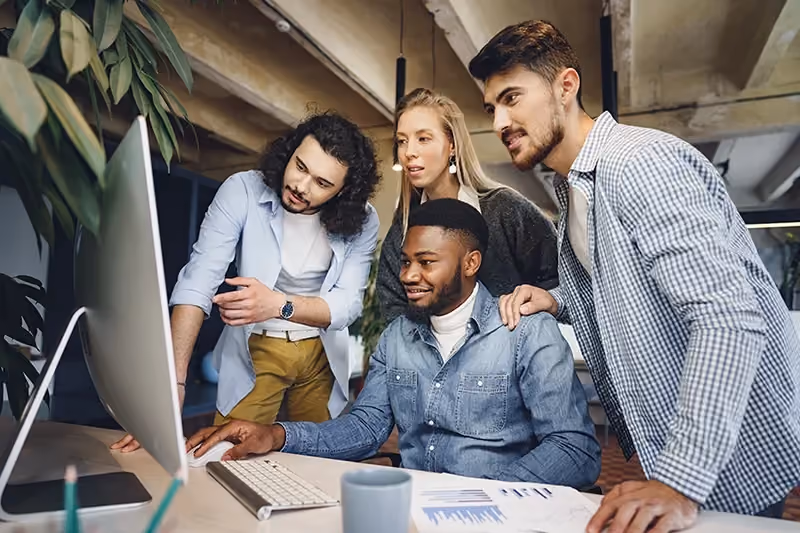 Um grupo de pessoas jovens, em volta de um computador, lendo sobre conteúdos de Procurement.