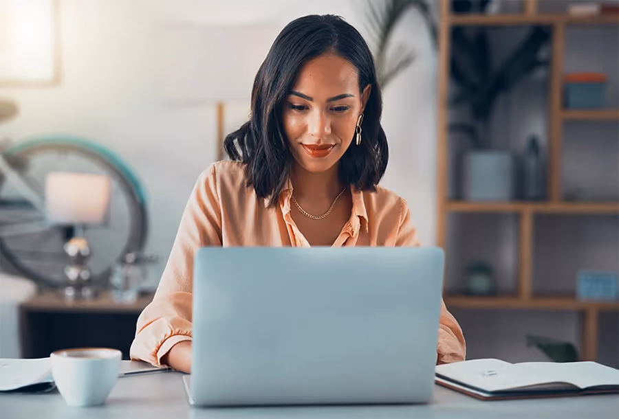 Mulher sorridente e lendo conteúdo sobre Gestão de Crédito B2B no seu laptop.
