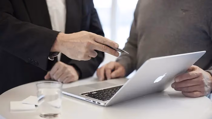 Pessoas em reunião, enquanto uma delas aponta para a tela de um computador.