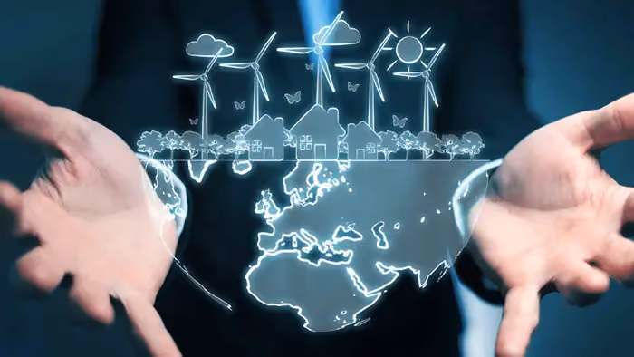 Mãos segurando holograma do planeta Terra com turbinas eólicas, casas e árvores, simbolizando sustentabilidade.