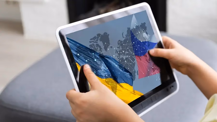 Uma pessoa usando um tablet com uma imagem de bandeiras da Ucrânia e Rússia ao centro.