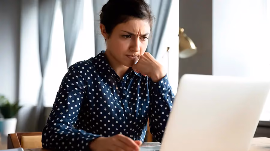 Mulher com o olhar confuso e preocupado e olhando para o computador.
