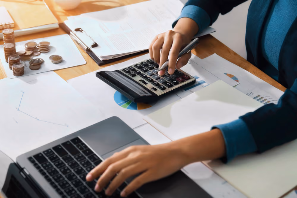 Mulher analisando gráficos no computador e calculadora, em processo de avaliação da regularidade fiscal da empresa