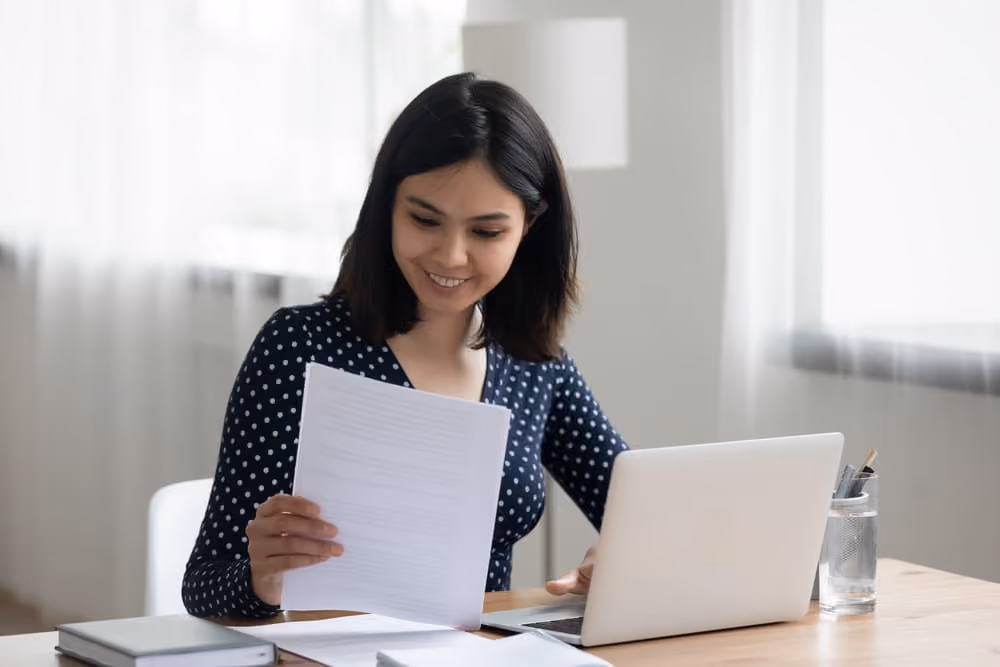 mulher com computador e documento em mãos, representando como emitir a Certidão Negativa de Débitos (CND)