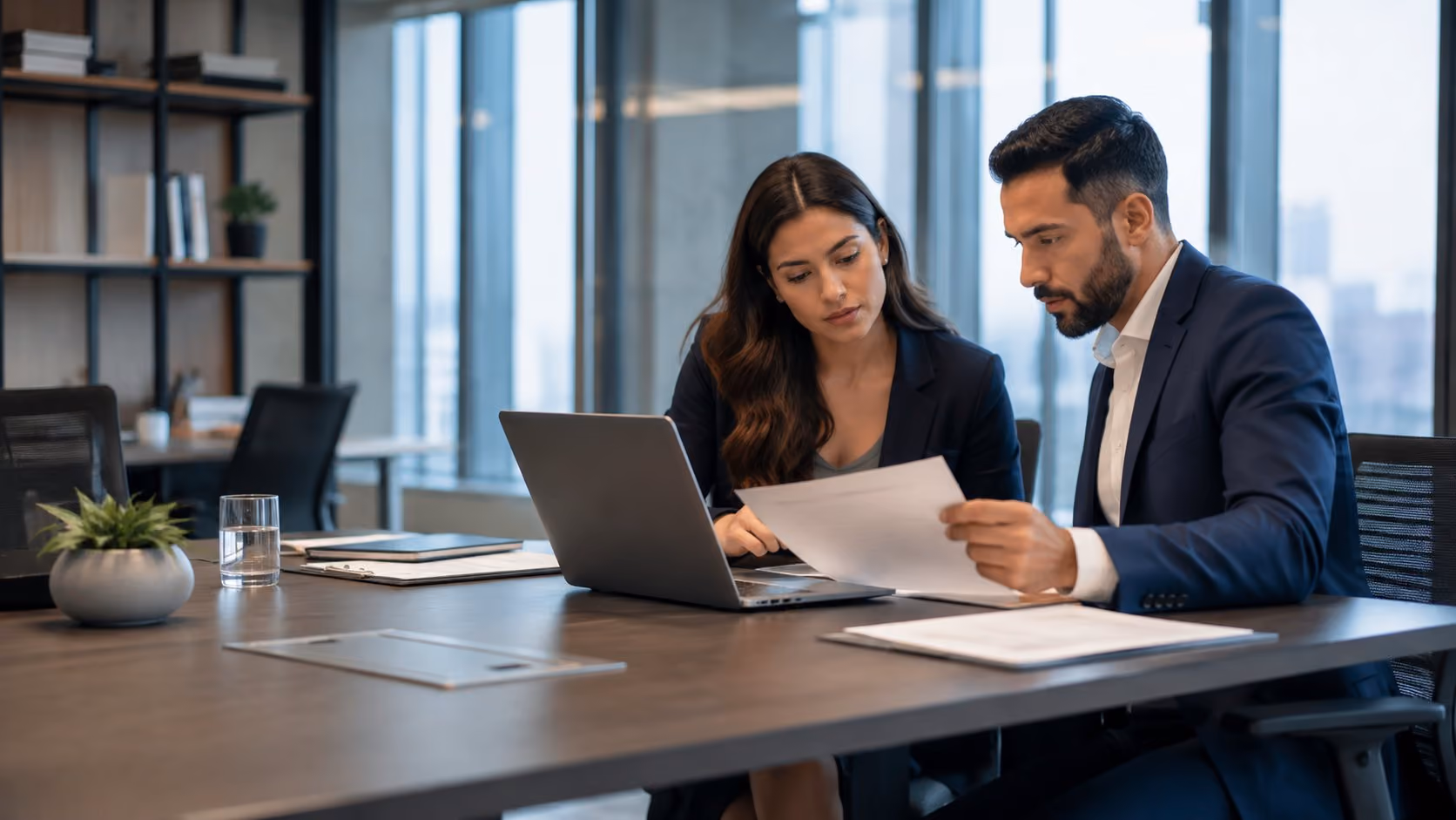 Profissionais em ambiente corporativo moderno analisando documentos e informações em notebook durante reunião de compliance.