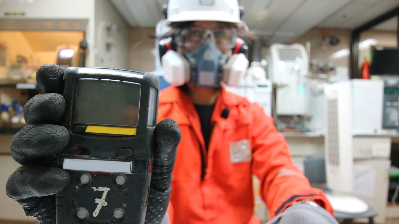 Profissional com EPI completo segura detector em ambiente industrial, representando mapeamento de riscos no trabalho.