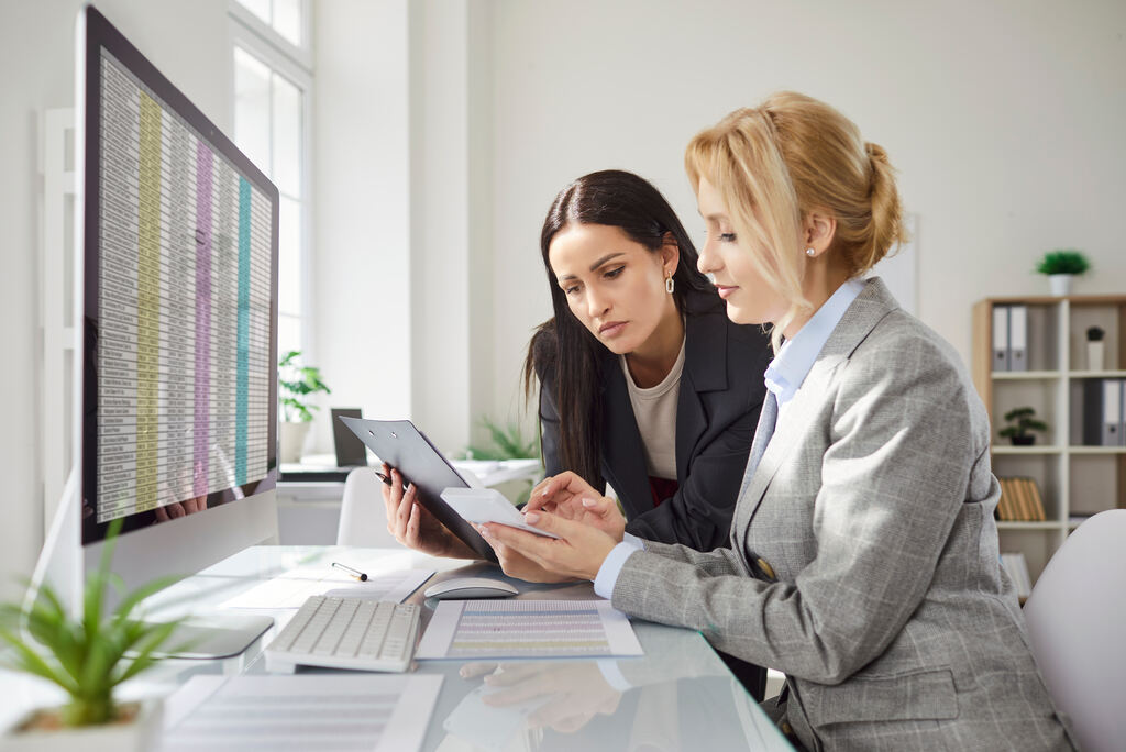 Profissionais avaliando dados financeiros e de compliance em telas e documentos.