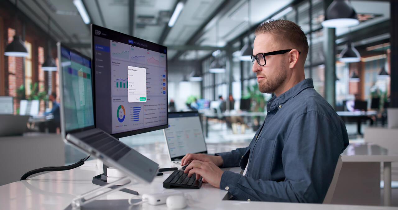 Profissional em escritório analisa dashboards em monitores para acompanhar automação de processos e indicadores de desempenho