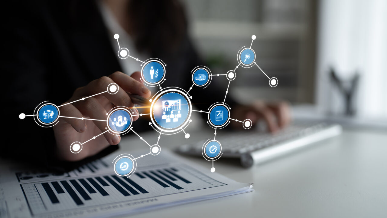 Pessoa trabalhando em mesa com teclado e documento de gráficos de barras, sobreposto por ícones digitais interconectados representando conceitos de planejmanto de contingência empresarial e tecnologia como análise de dados, trabalho em equipe e produtividade.