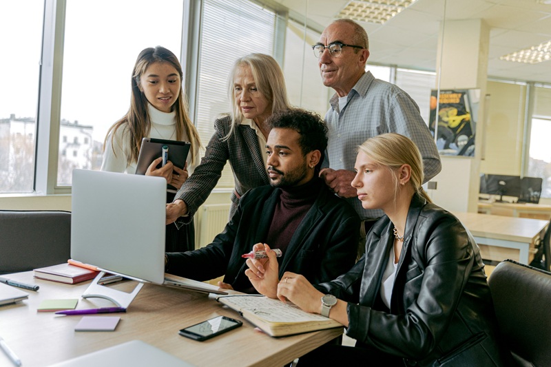 Equipe multigeracional reunida em torno de um notebook durante uma colaboração no escritório.