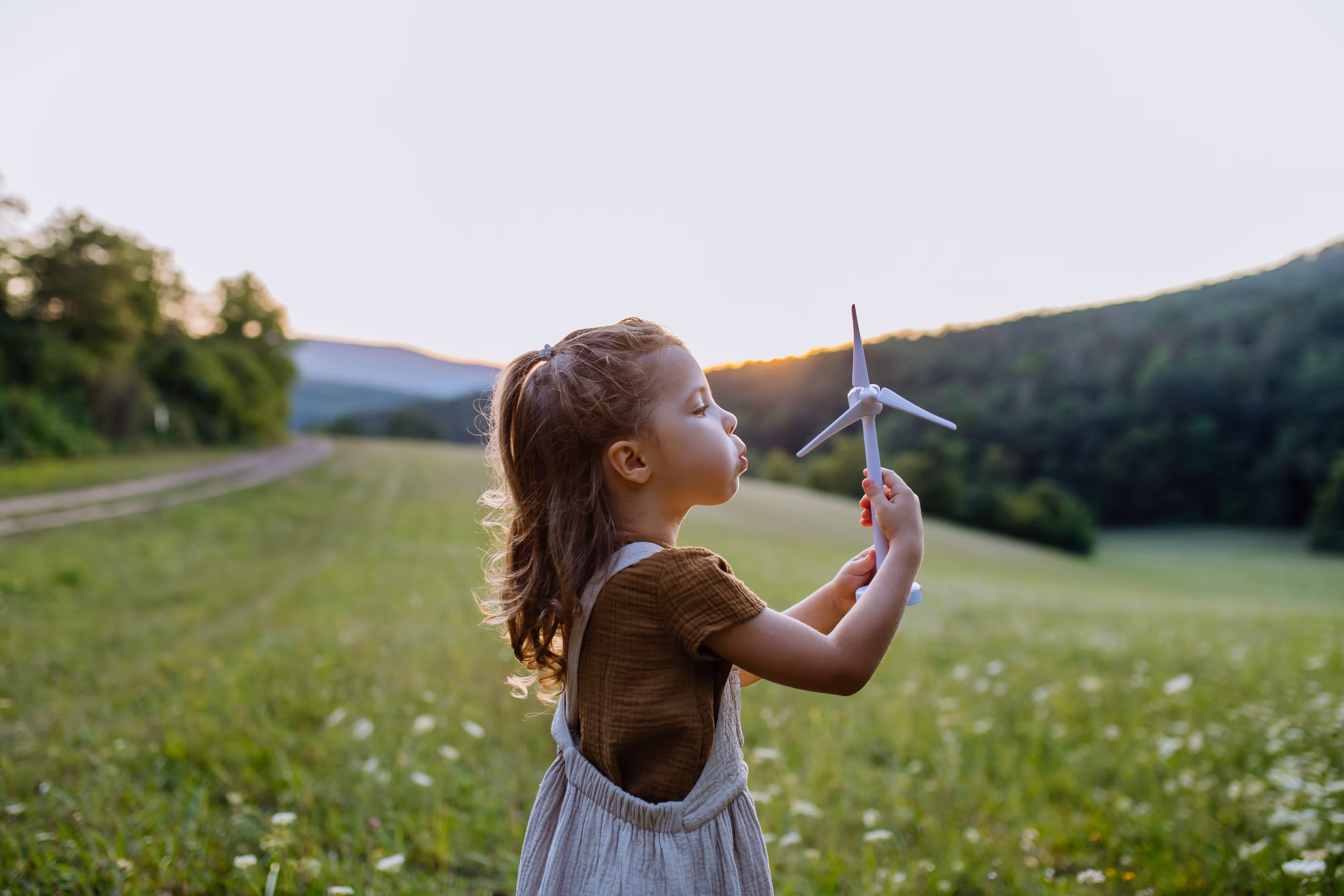 Little girl standing in nature with model of wind turbine. Concept of ecology future and renewable resources