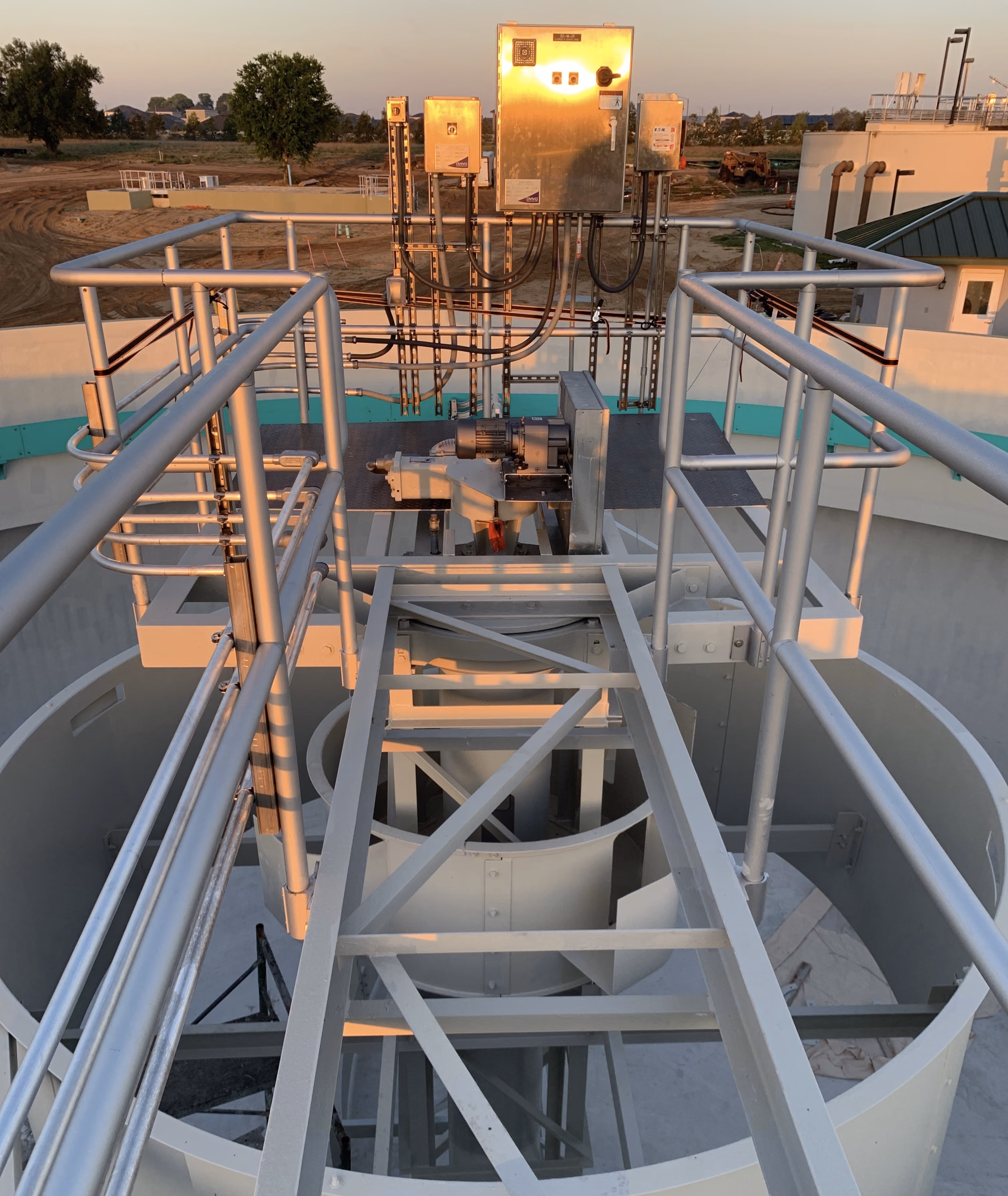 Industrial metal platform with railings and control boxes on top of a large cylindrical structure.